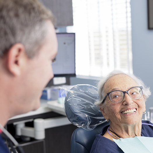 Senior woman in dental chair grinning at her dentist