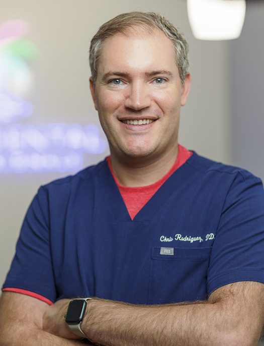 Doctor Christopher Rodriguez smiling in blue scrubs