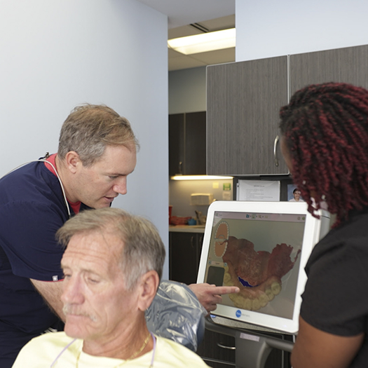 Dentist and assistant looking at a screen showing a digital model of a patients teeth